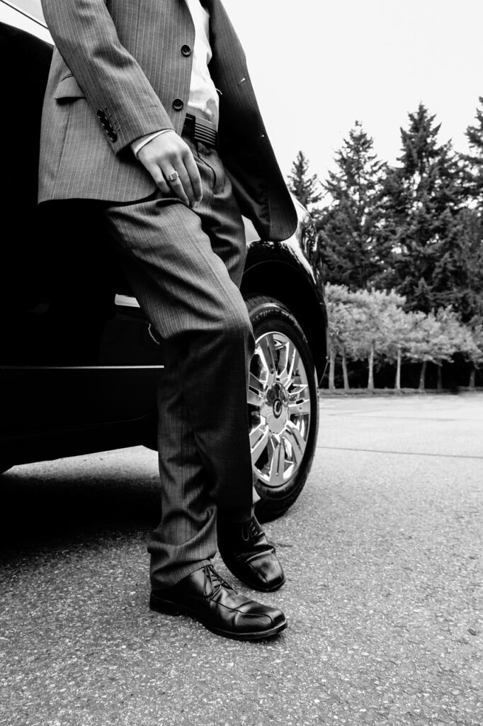 Chauffeur driver leaning by his car in a suit waiting for his vip customer