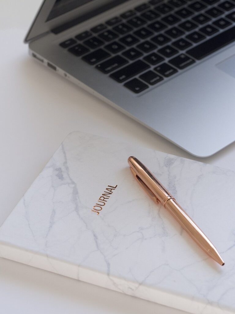 Gold pen laying on the side of paper next to a corner image of a laptop